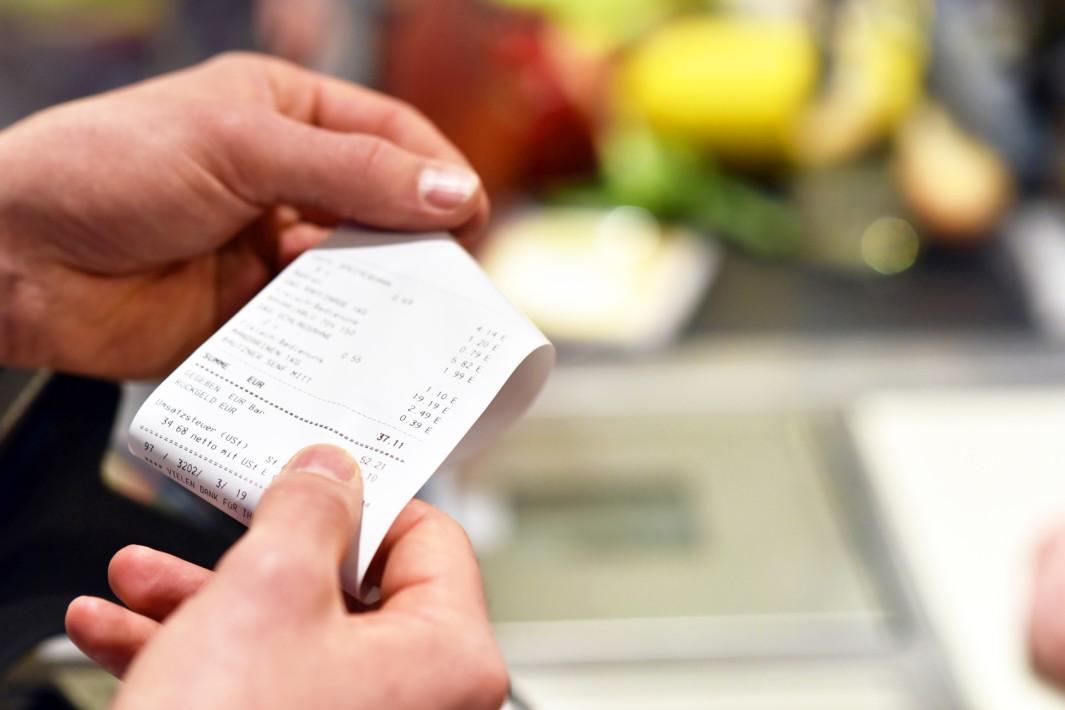 Hnde mit Kassenzettel an der Kasse im Supermarkt // hands with receipt at the checkout in the supermarket