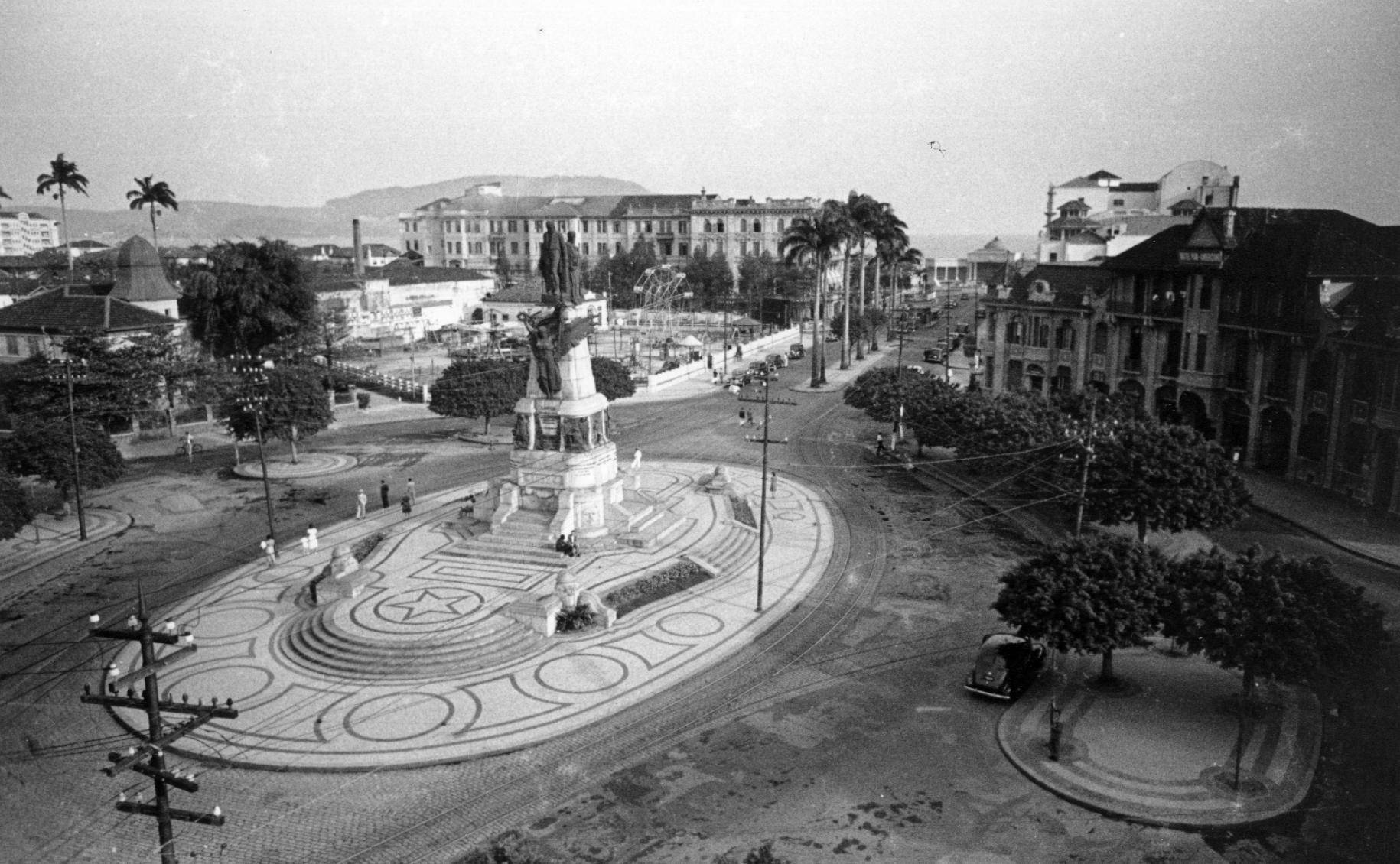Vista aérea em preto e branco da Praça da Independência em Santos, com monumento central, bondes e carros antigos.