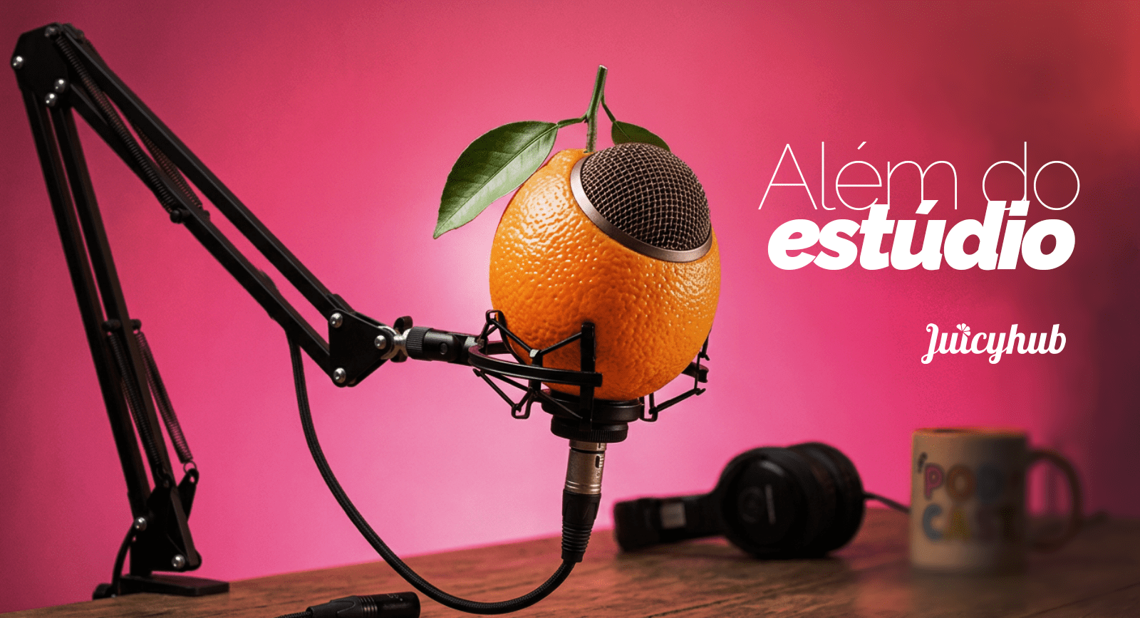 Laranja criativa com microfone em boom arm para podcast, fones, caneca e texto 'Além do estúdio Juicyhub' em fundo rosa.
