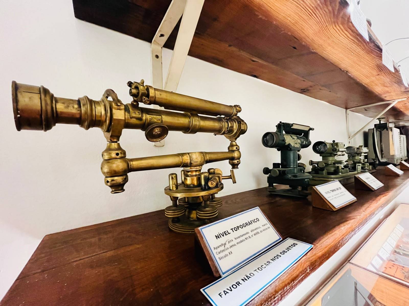 Exposição de níveis topográficos antigos e vintage em prateleira de madeira, incluindo um instrumento de latão e modelos Carlzeiss-Jema.