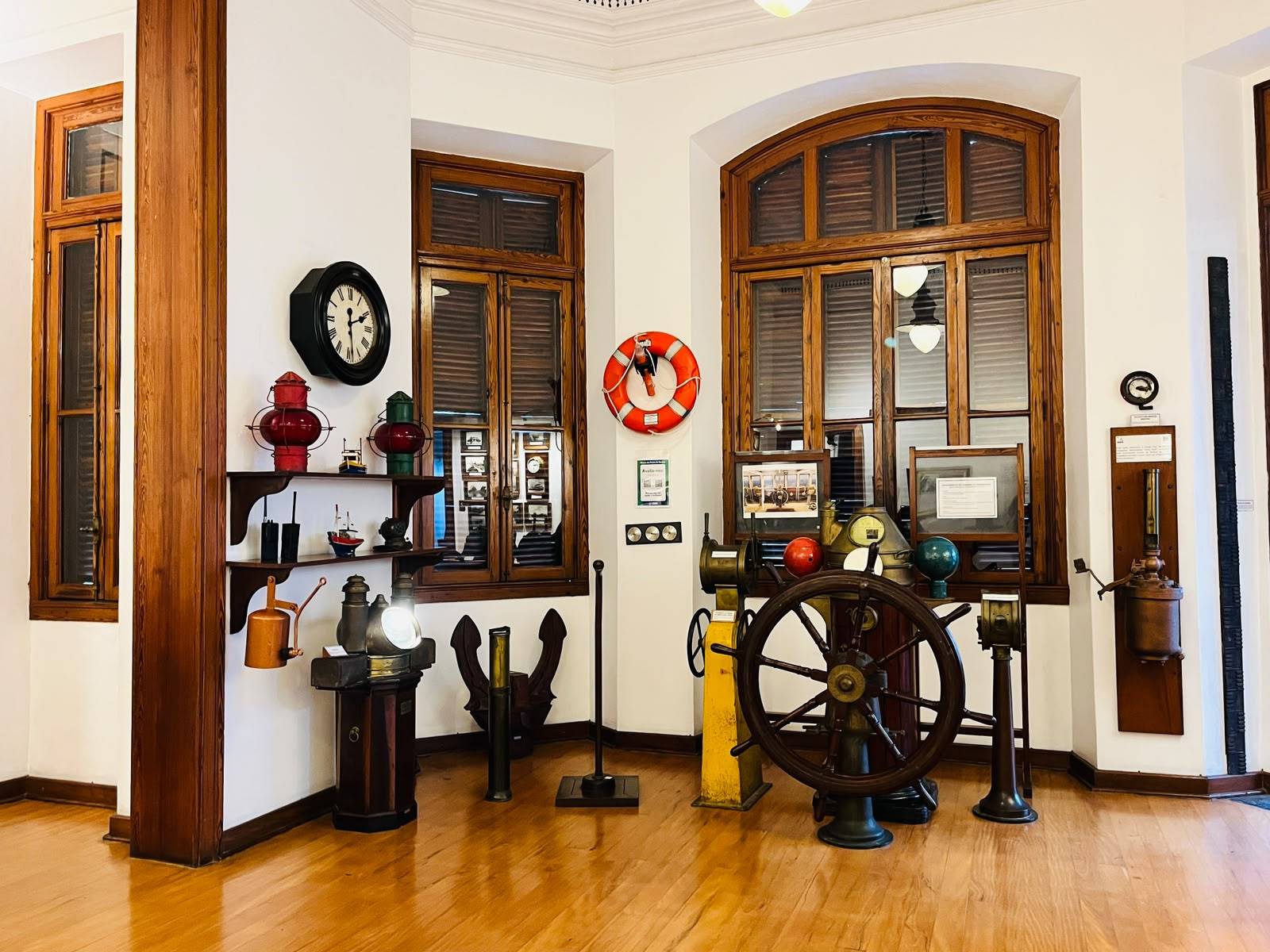 Interior de um museu marítimo com leme de navio, bóia salva-vidas e lanternas antigas em ambiente clássico.