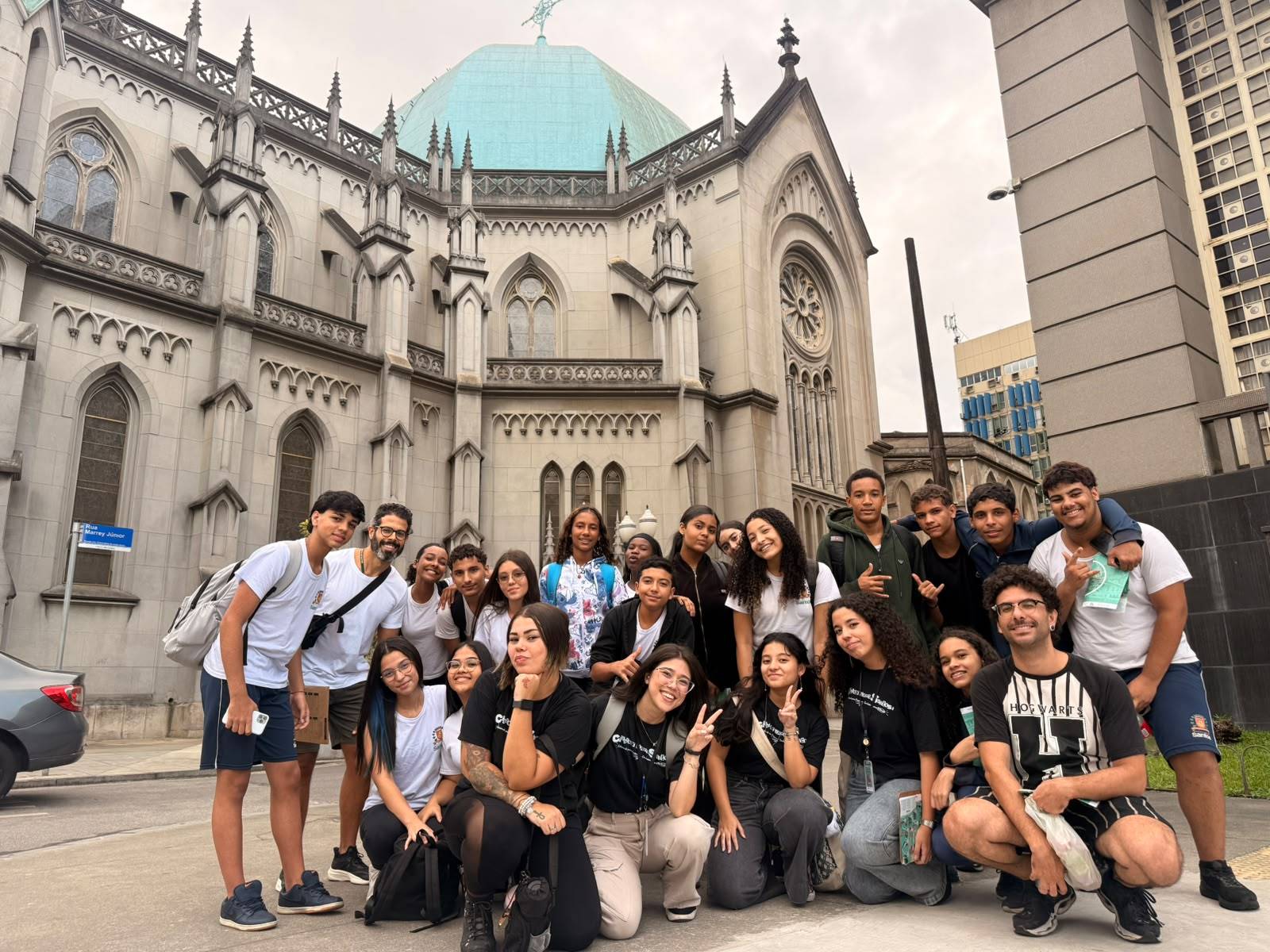 Grupo de jovens e adultos sorrindo em frente a uma igreja grandiosa com cúpula azul claro, em um passeio urbano.