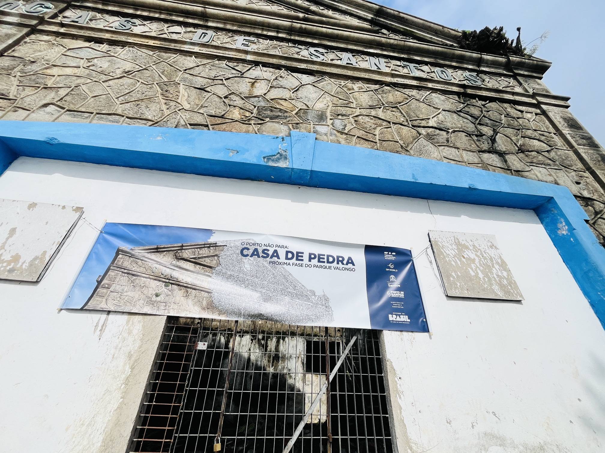 Fachada de um edifício de pedra histórico com guarnição azul e um banner 'Casa de Pedra: Próxima Fase do Parque Valongo'.