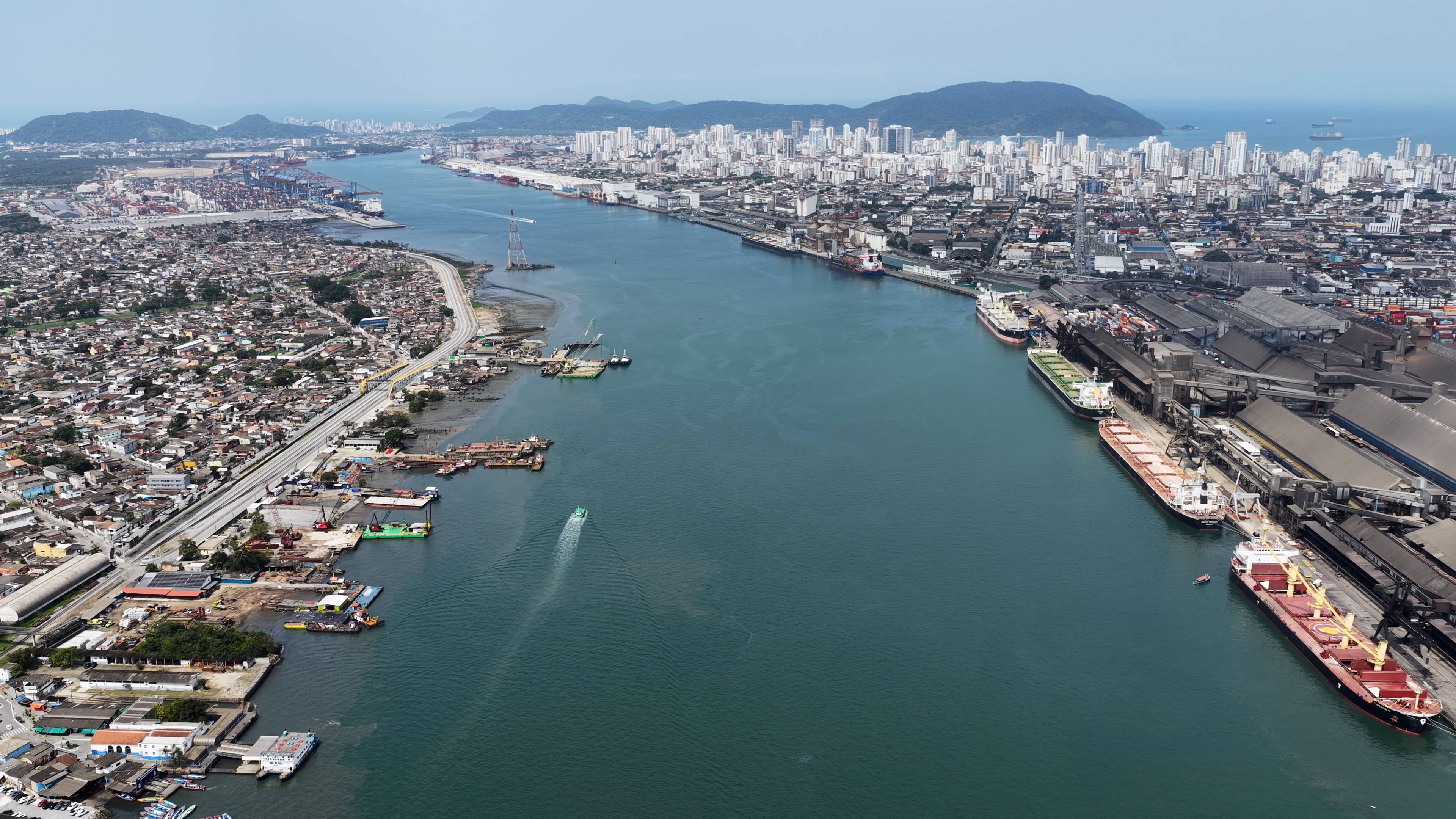 Vista aérea do complexo portuário de Santos, com navios, terminais de contêineres, áreas residenciais e skyline urbano.
