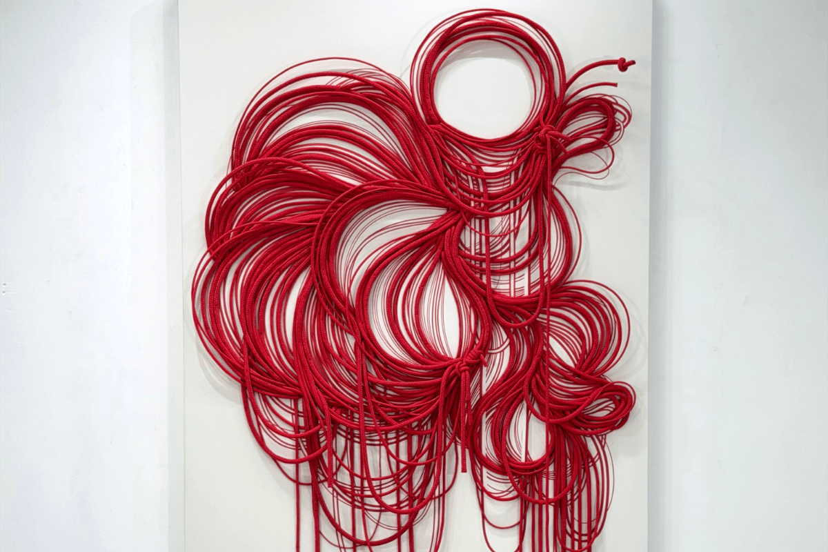 Escultura abstrata de cordas vermelhas vibrantes emaranhadas em espirais e formas orgânicas sobre um fundo branco.