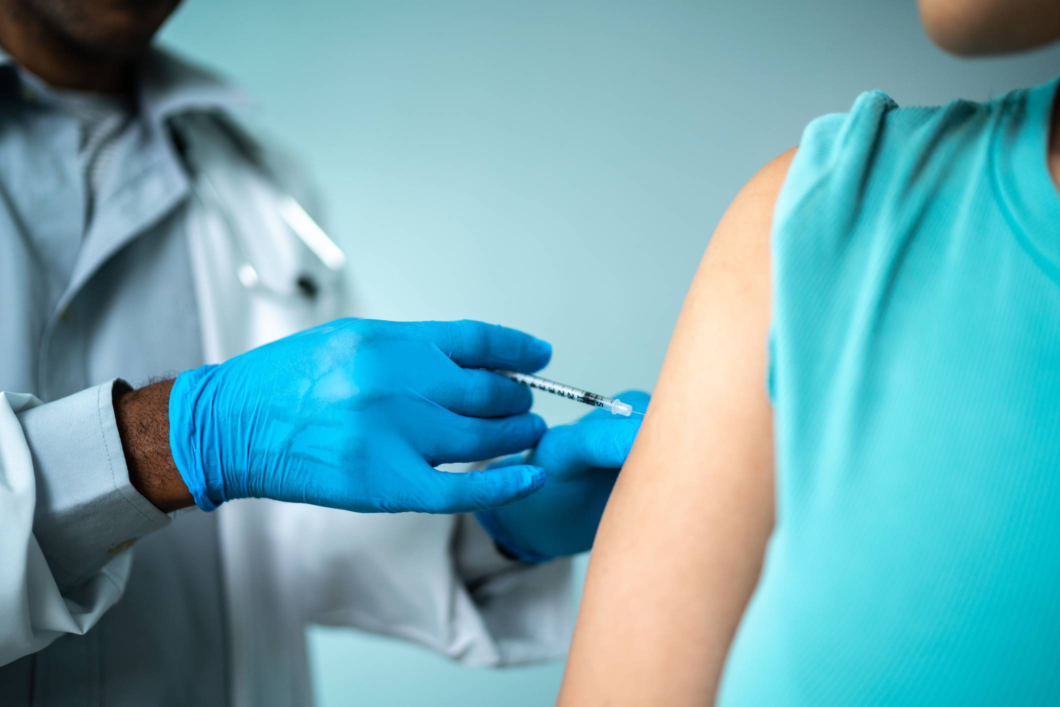 Profissional de saúde aplicando vacina ou injeção no braço de paciente com luvas azuis em ambiente clínico.