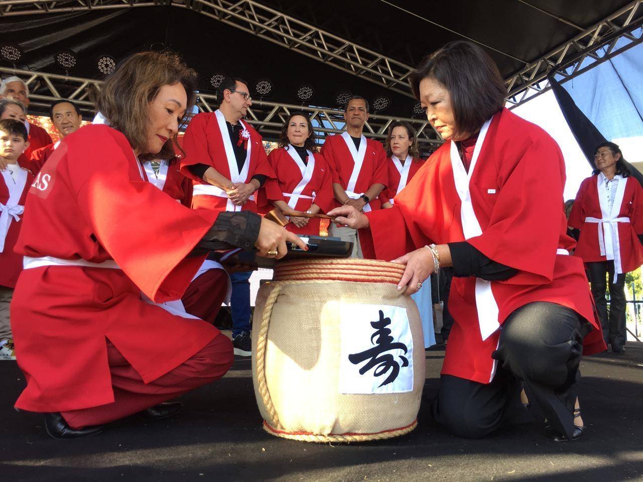 Duas mulheres em quimonos vermelhos quebram barril de saquê com malhos no ritual Kagami Biraki em palco