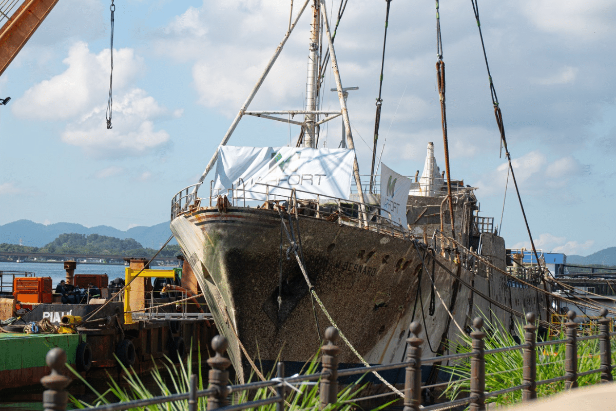 Navio antigo e enferrujado, W. Besnard, atracado em doca com banners 'MARFORT' e guindaste, ao lado de barcaça 'Piaui'.