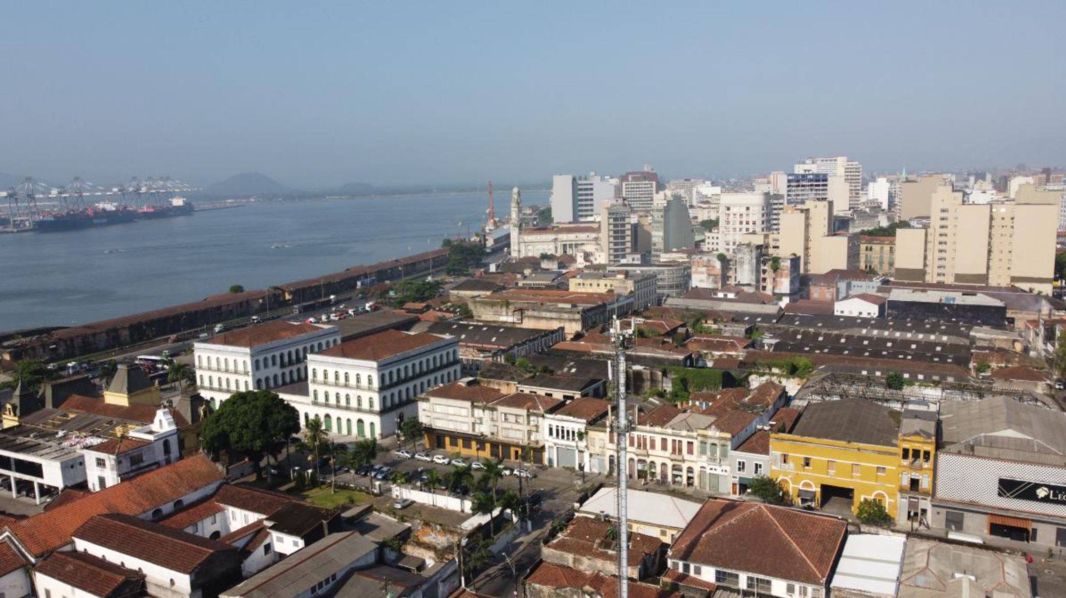 Vista aérea do porto de Santos com navios, guindastes e prédios históricos próximos à orla