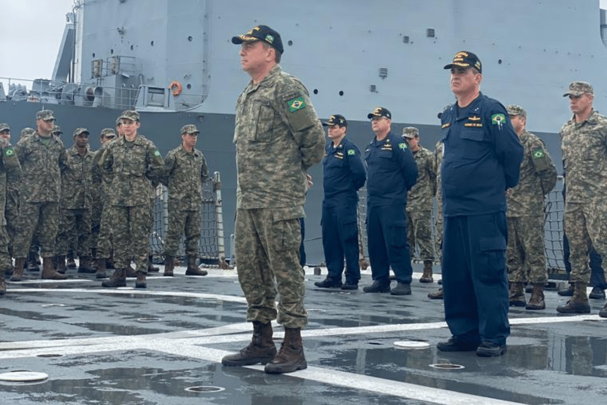Militares brasileiros em uniforme de camuflagem e azul-marinho formados no convés de um navio, com oficiais de alta patente.